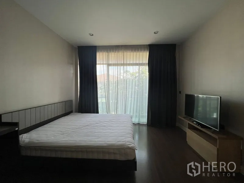 Detached House for rent or sale in Bang Kapi, Bangkok - Bedroom with large window, bed and TV console facing a glass door to the garden.