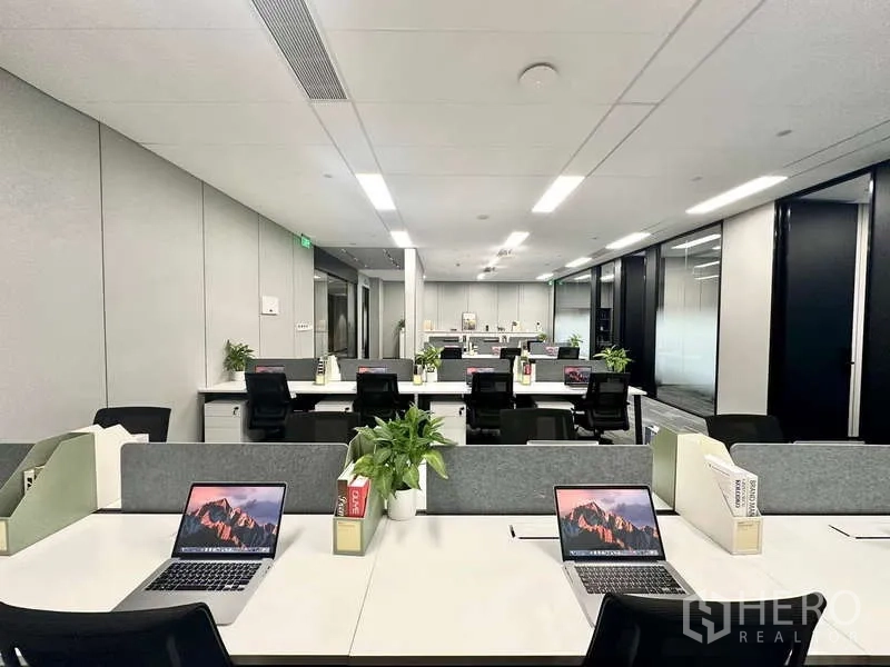 Office Space for rent in Bang Kapi, Bangkok - Modern open‑plan office with rows of workstations, grey partitions, laptops and potted plants under LED lighting.