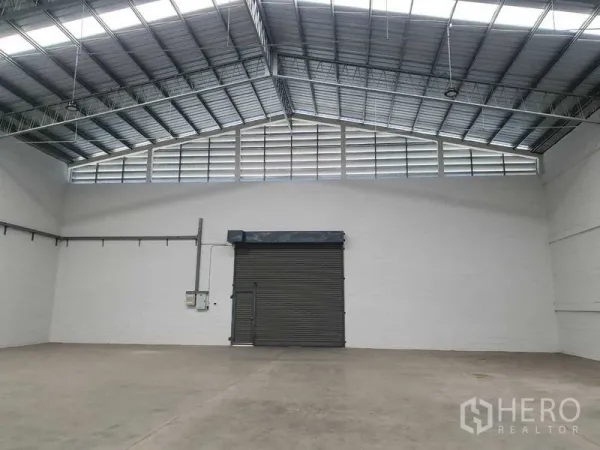 货栈 出租在Khlong Luang, Pathum Thani - 仓库端墙配大卷闸门、上部百叶窗与电力配电箱。