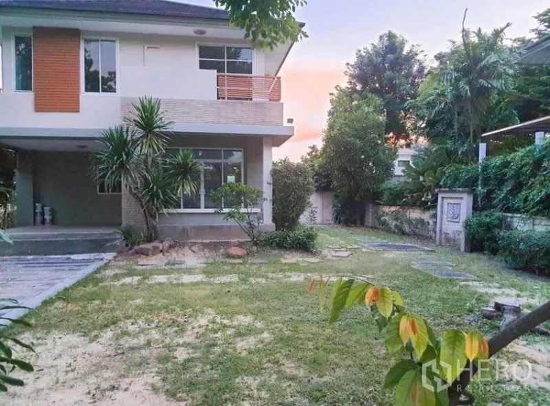 Detached House for sale in Saphan Sung, Bangkok - Two-storey house exterior with a large green garden, trees and boundary wall at sunset.