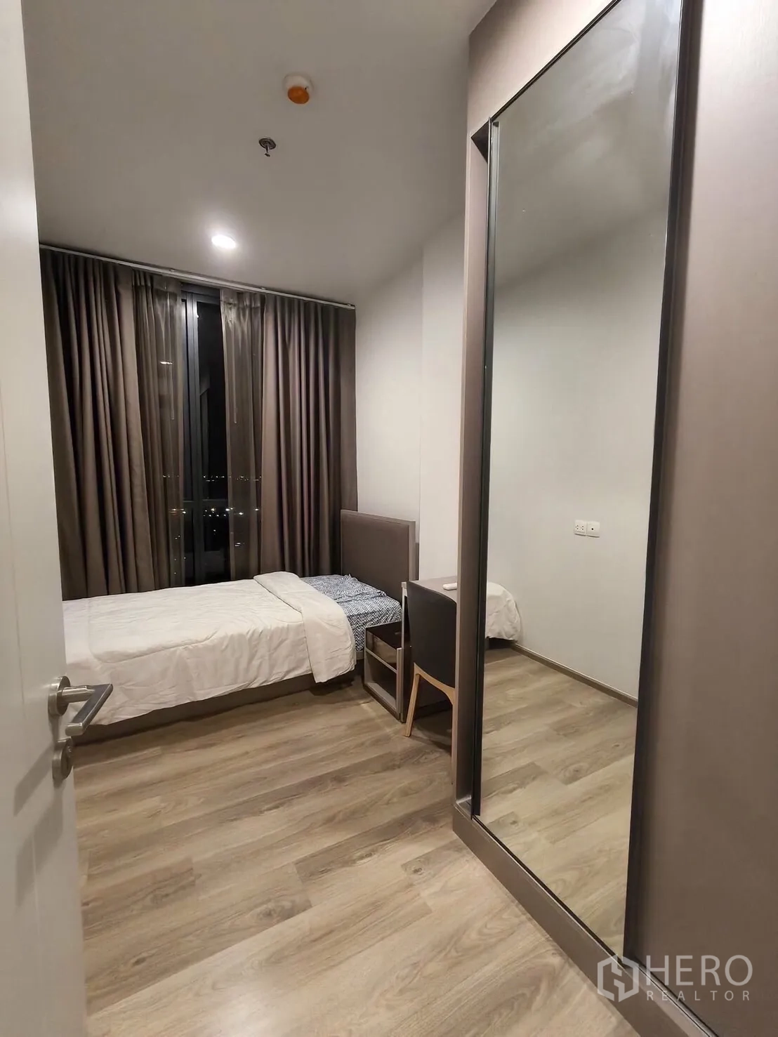 Condominium for rent in Khlong Toei, Bangkok - Second bedroom with a single bed, study desk, and full-height mirrored wardrobe beside a window.