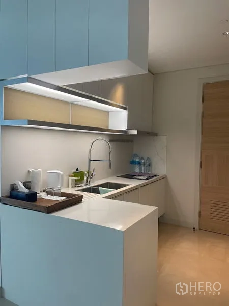 Condominium for rent in Pathum Wan, Bangkok - Sleek kitchen with white cabinetry, peninsula counter and under-cabinet lighting.