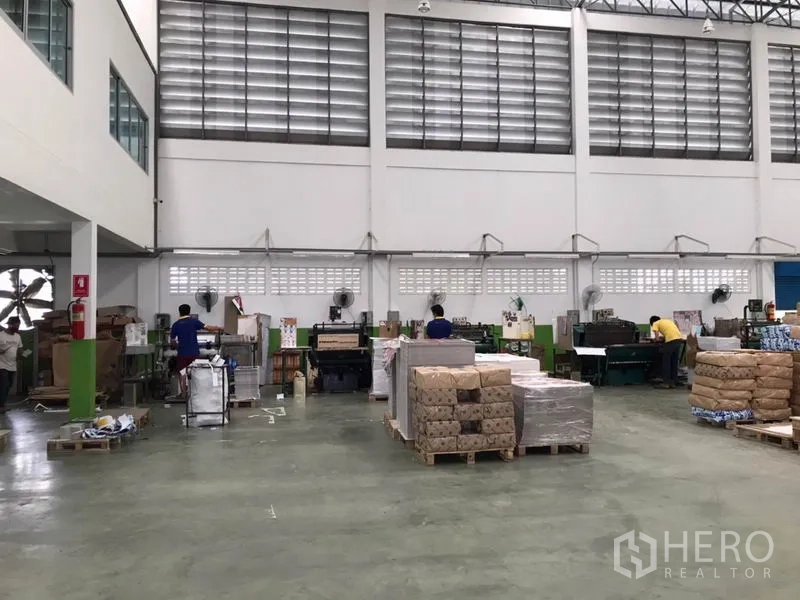 Factory for sale in Pak Kret, Nonthaburi - Open production floor with high louvered windows, machinery, and stacked pallets.