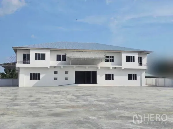 Warehouse for rent in Mueang Samut Prakan, Samut Prakan - Two-storey warehouse building with an expansive paved yard for truck parking.