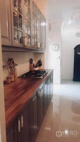 Townhouse for rent or sale in Bangkok - Galley kitchen featuring wooden countertop, gas hob and glass-front cabinets with bright flooring.