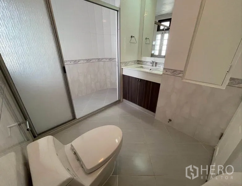 公寓 出租在Watthana, Bangkok - 浴室，玻璃淋浴间、带镜洗手台与瓷砖墙面。
