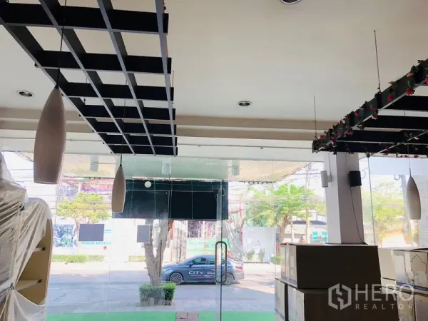 店屋 出租在Lat Phrao, Bangkok - 整面落地玻璃店面朝向街道，黑色格栅天花与吊灯。