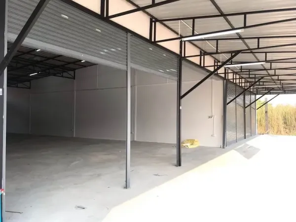 Warehouse for rent in Lam Luk Ka, Pathum Thani - Loading area with multiple open roller shutters under a metal canopy and wide driveway.