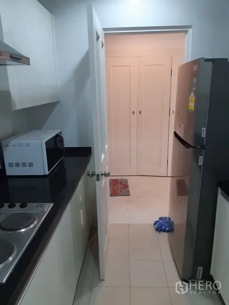 Condominium for rent in Khlong Toei, Bangkok - Compact kitchen view showing electric cooktop, range hood and microwave.