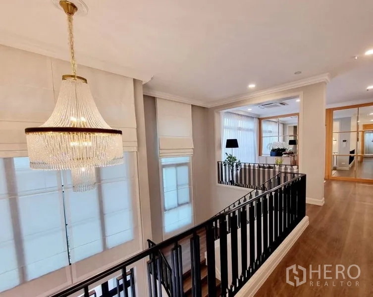 Detached House for rent in Saphan Sung, Bangkok - Upper hallway with crystal chandelier, black balustrade, and wood floors.