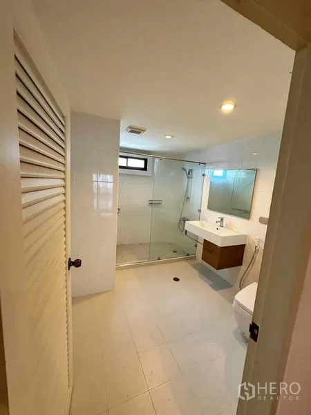 Condominium for rent in Bangkok - Bright bathroom featuring a glass-enclosed shower, wall-hung vanity and toilet.