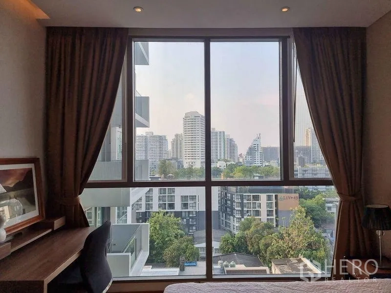 公寓 出租在Watthana, Bangkok - 卧室窗外城市天际线景观，可见低层建筑与绿树。