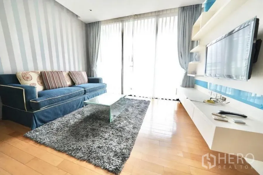 Condominium for rent or sale in Watthana, Bangkok - Living room with floor-to-ceiling windows, wall-mounted TV and glass coffee table.