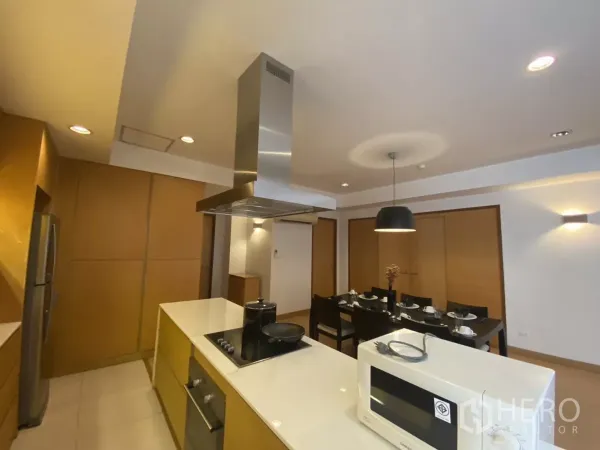Condominium for rent in Watthana, Bangkok - Modern kitchen with island cooktop, stainless hood and microwave overlooking the dining area.