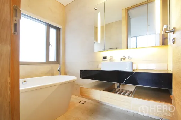 Condominium for sale in Bang Rak, Bangkok - Spa-style bathroom featuring a freestanding bathtub, large mirror and black stone vanity.