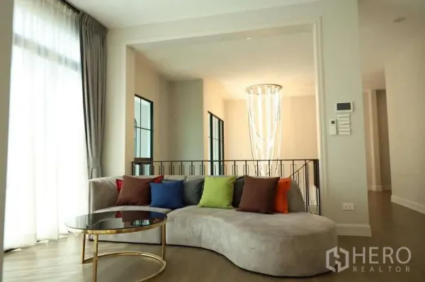 Detached House for rent or sale in Saphan Sung, Bangkok - Bright sitting area with curved sofa, colorful pillows and chandelier by stairs.
