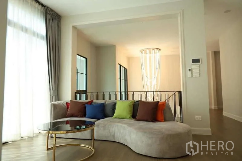 Detached House for rent or sale in Saphan Sung, Bangkok - Bright sitting area with curved sofa, colorful pillows and chandelier by stairs.