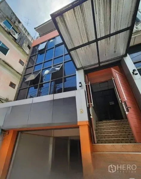 办公空间 出租或出售在Bueng Kum, Bangkok - 曼谷Bueng Kum现代低层办公楼，玻璃立面与橙色点缀，设有遮雨棚和入口楼梯。