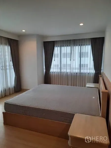 Condominium for rent in Watthana, Bangkok - Spacious bedroom with corner windows, double bed, bedside tables and floor-to-ceiling curtains.