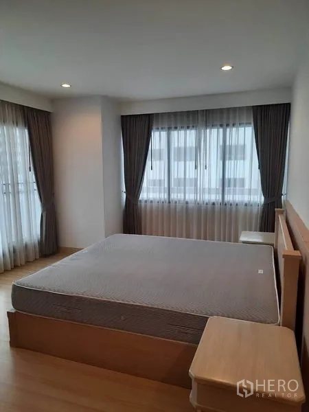 Condominium for rent in Watthana, Bangkok - Spacious bedroom with corner windows, double bed, bedside tables and floor-to-ceiling curtains.