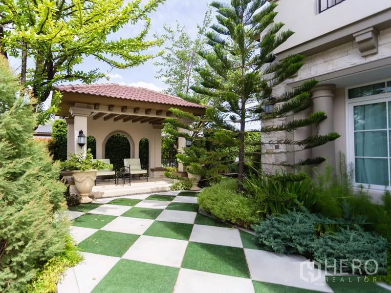 Detached House for rent in Mueang Samut Prakan, Samut Prakan - Landscaped garden with checkered patio and a covered pavilion seating area beside mature trees.