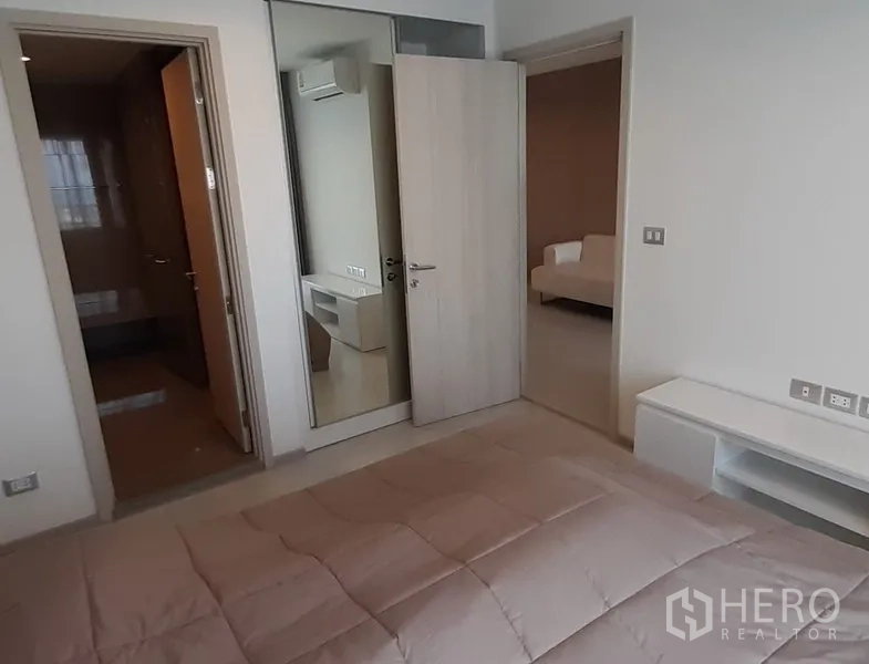 Condominium for rent in Khlong Toei, Bangkok - Bedroom with mirrored wardrobe, door to ensuite bathroom, and view toward the living room.