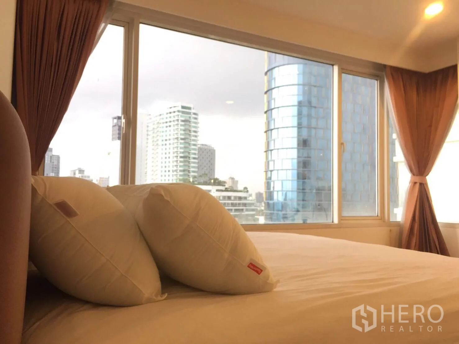 Condominium for rent in Watthana, Bangkok - Master bedroom with large windows, city view and warm curtains over a neatly made bed.