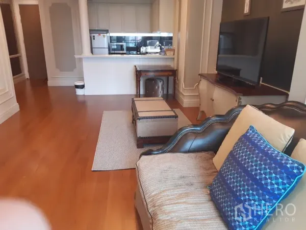 Condominium for rent in Khlong Toei, Bangkok - Open-plan living area facing a breakfast-bar kitchen with hardwood flooring and TV unit.
