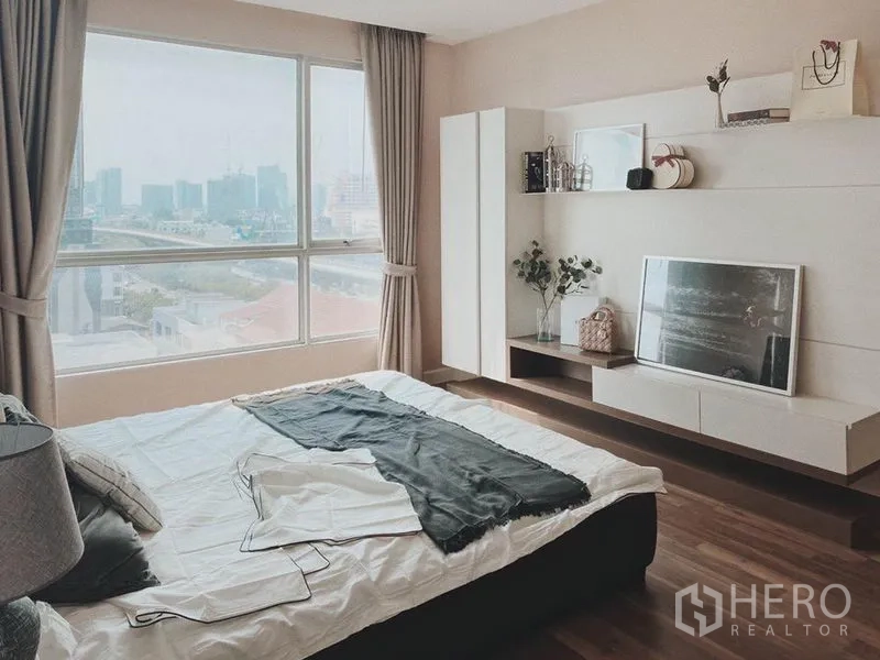 Condominium for rent in Thon Buri, Bangkok - Master bedroom with panoramic window, wood floors and built-in shelving.