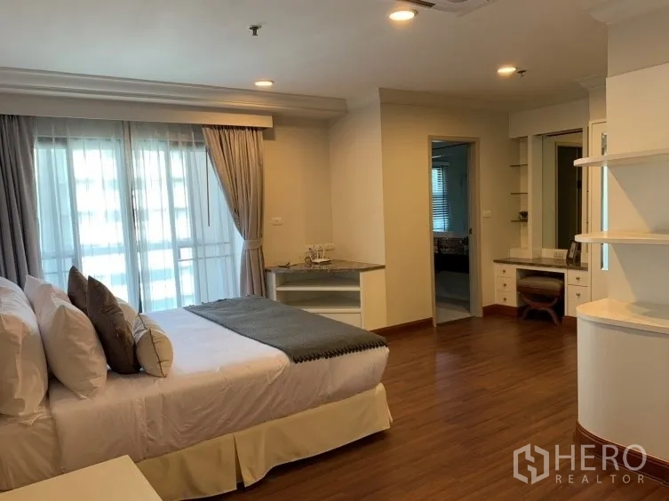 Condominium for rent in Watthana, Bangkok - Bright bedroom with king bed, sheer-draped balcony doors, wood flooring, and built-in desk.