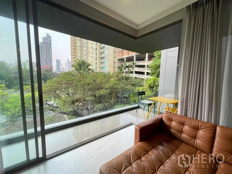 公寓 出租或出售在Watthana, Bangkok - 客厅转角，宽幅玻璃与阳台外的城市与绿景。