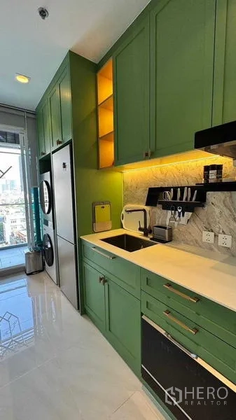 Condominium for rent in Bang Rak, Bangkok - Modern galley kitchen with green cabinetry, marble backsplash, under-cabinet lighting and sink beside a bright window.