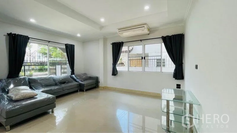 Detached House for rent in Bang Kapi, Bangkok - Bright living room with L-shaped sofa, glass side table, large windows and air conditioning.
