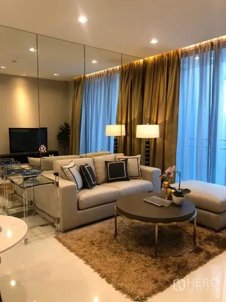 Condominium for rent in Khlong Toei, Bangkok - Cozy lounge with floor-to-ceiling curtains, sofa, round coffee table and soft lighting.