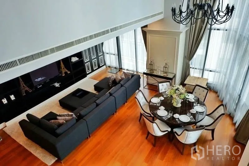 Condominium for rent in Khlong Toei, Bangkok - Aerial view of open-plan lounge and dining space with floor-to-ceiling windows, hardwood floors and a black chandelier.