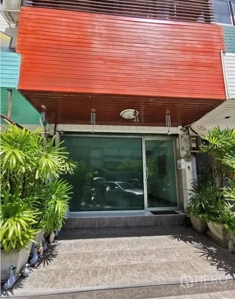 สำนักงาน ให้เช่าในHuai Khwang, Bangkok - ทางเข้าอาคารสำนักงานกระจก ชั้นล่าง พร้อมซุ้มไม้สีแดงและกระถางต้นไม้ ในห้วยขวาง.