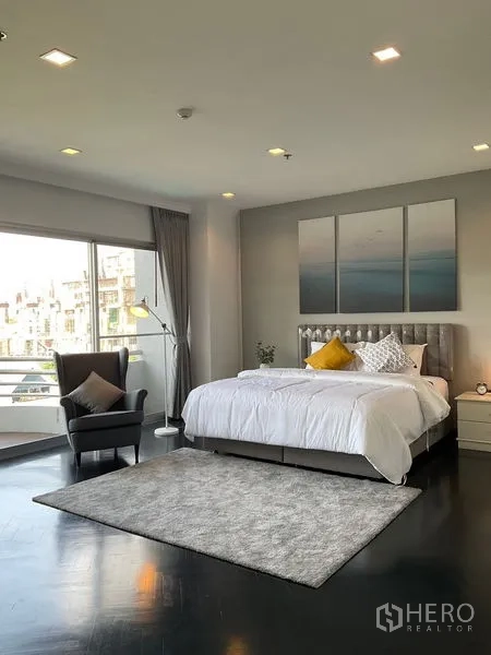 Apartment for rent in Sathon, Bangkok - Sunlit bedroom with armchair, rug and direct balcony access.