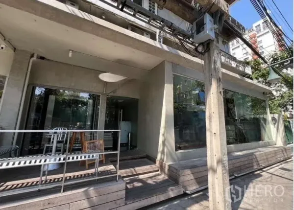 Shophouse for rent in Watthana, Bangkok - Street-level shophouse exterior in Watthana with large glass storefront and shaded wooden terrace.