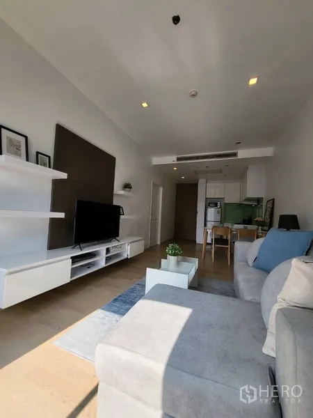 Condominium for rent in Bangkok - Bright living room with L-shaped sofa, TV wall and floating shelves in a modern condo.