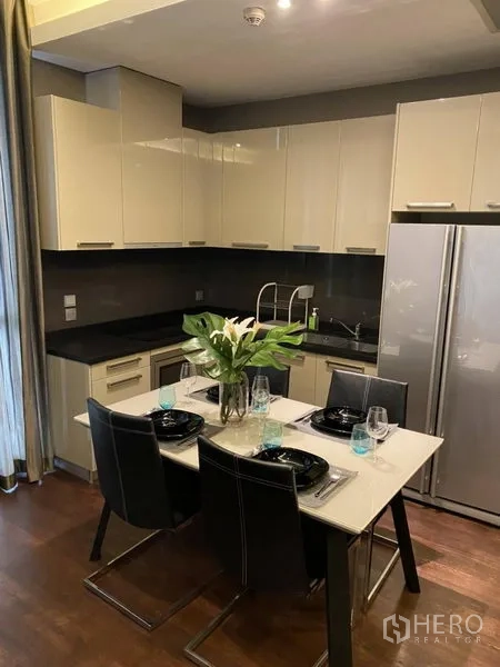 Condominium for rent in Watthana, Bangkok - Compact modern kitchen with glossy cabinets, black countertops, double-door fridge and a dining table set for four.