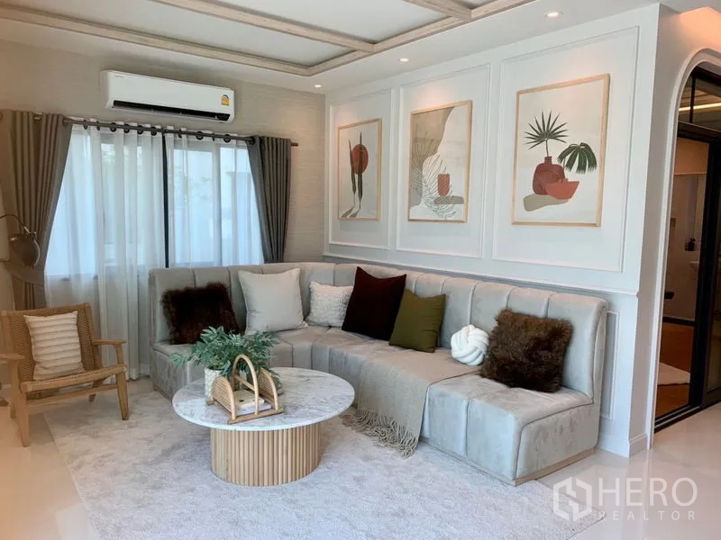 Detached House for sale - Family lounge with L-shaped sofa, round coffee table, wall art panels and curtained windows.