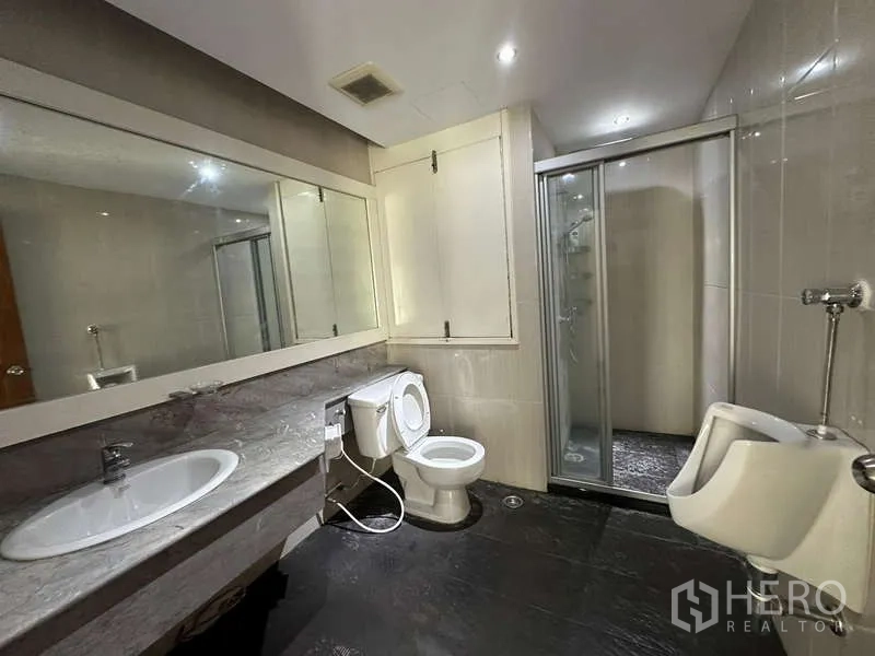公寓 出租在Watthana, Bangkok - 宽敞浴室，超大镜面、洗手台、坐便器、小便器及玻璃淋浴间。