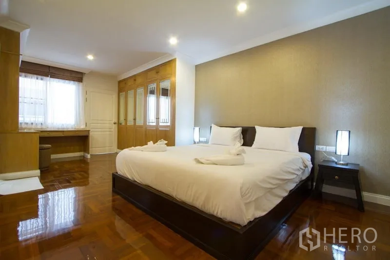 Apartment for rent in Watthana, Bangkok - Large bedroom with king bed, mirrored wardrobes, wood floors, and soft downlights.
