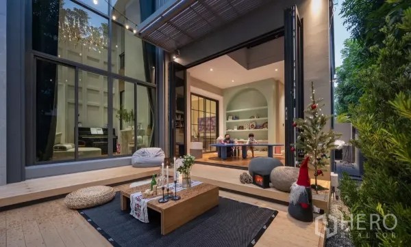 Detached House for rent or sale in Phra Khanong, Bangkok - Outdoor terrace opening to a playroom via folding doors, with timber deck, string lights and a tall glass wall.