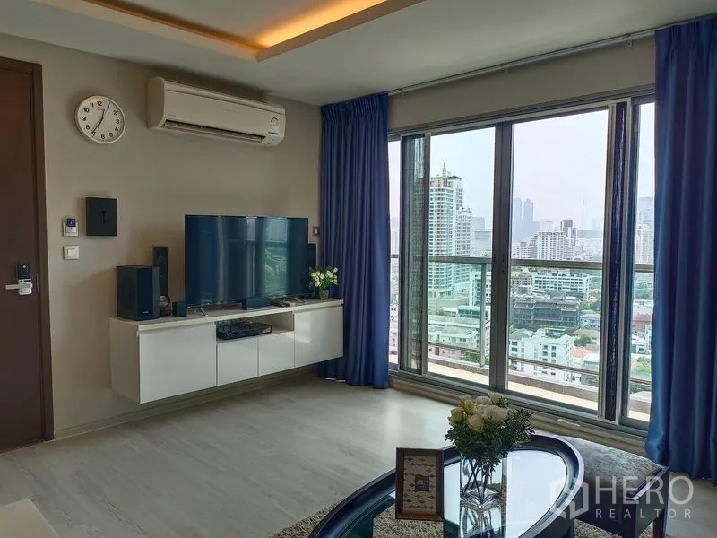 Condominium for rent in Watthana, Bangkok - Living room with TV console and floor-to-ceiling windows opening to a balcony city view.