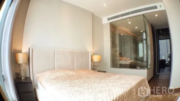 Condominium for rent in Khlong Toei, Bangkok - Bright master bedroom with padded headboard and glass-walled en-suite bathroom.