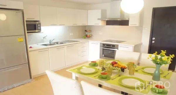 Apartment for rent in Khlong Toei, Bangkok - Modern white kitchen with built-in oven, microwave, large fridge and a four-seat dining table under pendant light