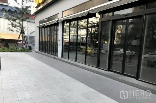 Retail Space for rent in Khlong Toei, Bangkok - Ground-floor retail unit with full-height glass frontage, dark frames, awnings, and a wide paved forecourt near BTS Thonglor.