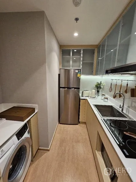 Condominium for rent - Galley kitchen with induction hob, hood, fridge and washer, light wood cabinets.