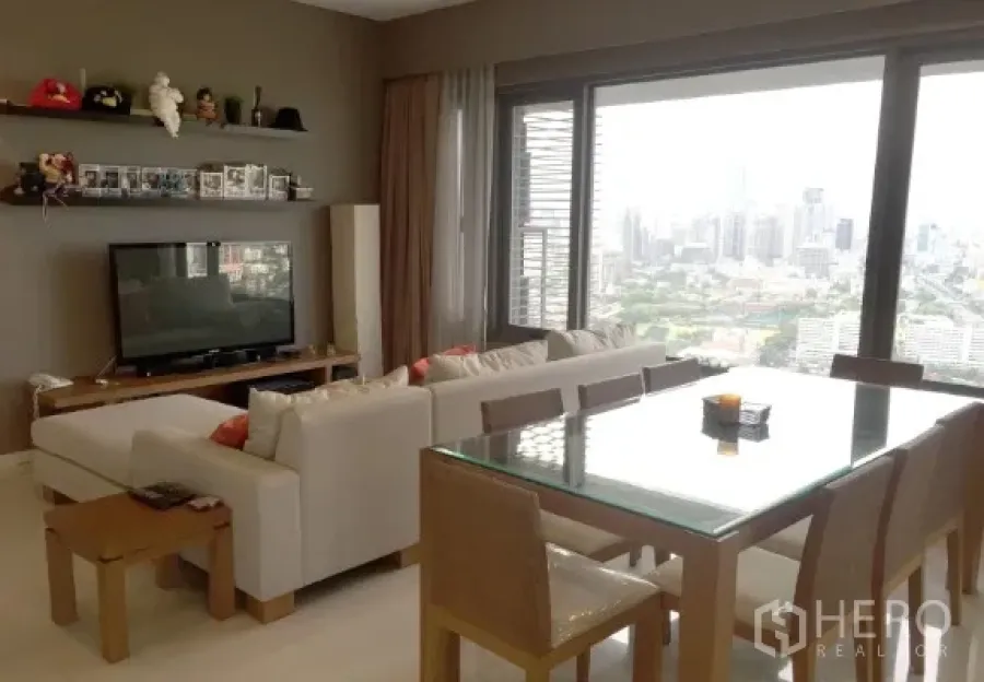 公寓 出租或出售在Sathon, Bangkok - 客厅电视区与玻璃餐桌，整面落地窗对望天际线与大片绿地景观。